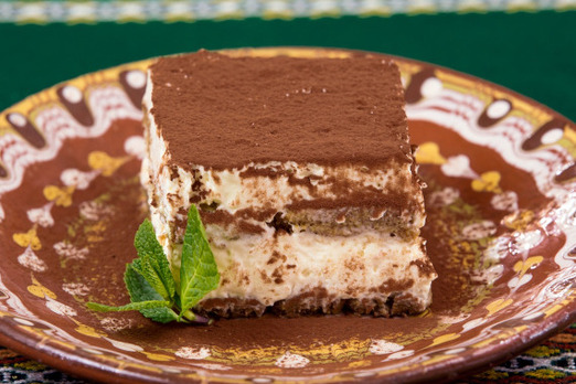 Cremiges Tiramisu mit Kakaopulver und Minze auf einem dekorativen Teller angerichtet